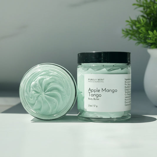 Two jars of Apple Mango body butter on a white counter with a green plant.