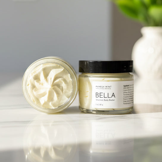 Two jars of Bella Shimmer body butter on a white marble counter with a green plant in a white vase.