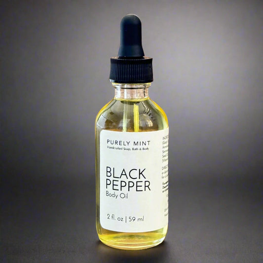 Black Pepper Body Oil, clear glass bottle, white label, black dropper top, commercial photography packshot, dark gray seamless backdrop.