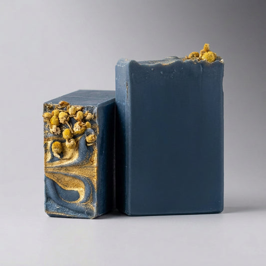 Two Black chamomile artisan soaps with decorative tops on a light gray backdrop..