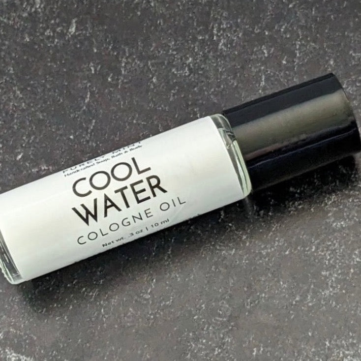 Mens Cologne Oil Roll On. A clear glass roll-on bottle with a black cap. The bottle is labeled 'PURELY MINT Hand-Crafted Soaps, Bath & Body COOL WATER COLOGNE OIL'