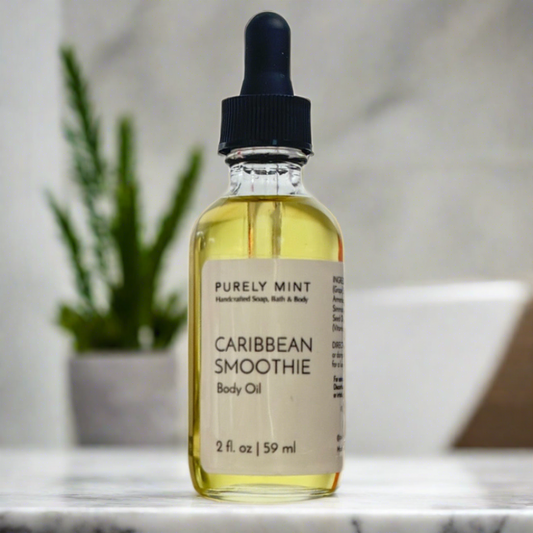 A bottle of Caribbean Smoothie Hydrating Body Oil with a dropper, labeled with the product name and volume, placed on a surface with a plant in the background.