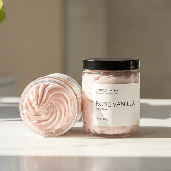 Jar of 'Rose Vanilla' body butter on a bathroom counter with a potted plant in the background.