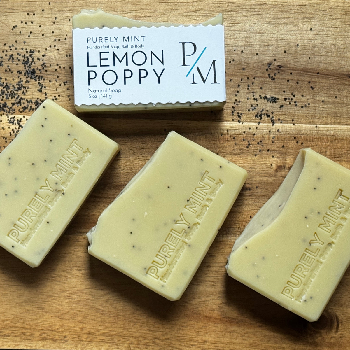Four bars of Lemon Poppy Natural Soap by Purely Mint on a wooden surface with one labeled Lemon Poppy.