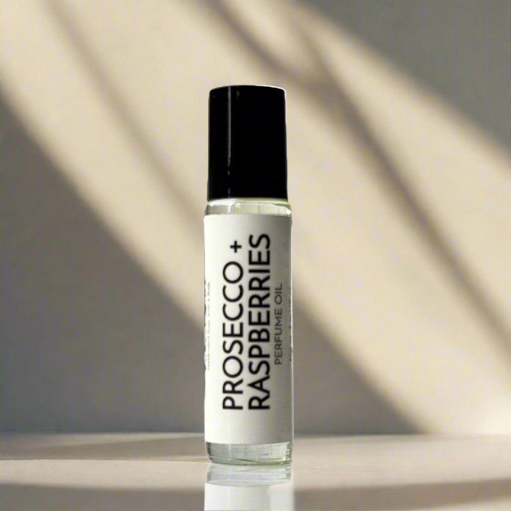 Perfume oil bottle labeled 'Prosecco + Raspberries' on a light tan background