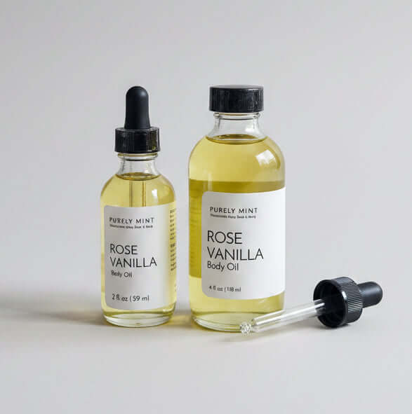 Two glass bottles of Rose Vanilla Body Oil with black dropper caps, standing on a light gray seamless backdrop.