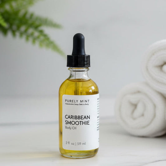 Bottle of Caribbean Smoothie body oil on a white marble counter green plant rolled white wash clothes.