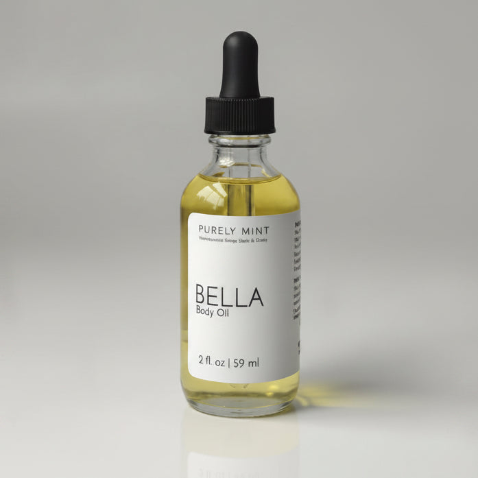A small glass dropper bottle with pale yellow liquid and a black dropper cap, standing on a light gray backdrop. The label reads  'Purely Mint Bella Body Oil'.