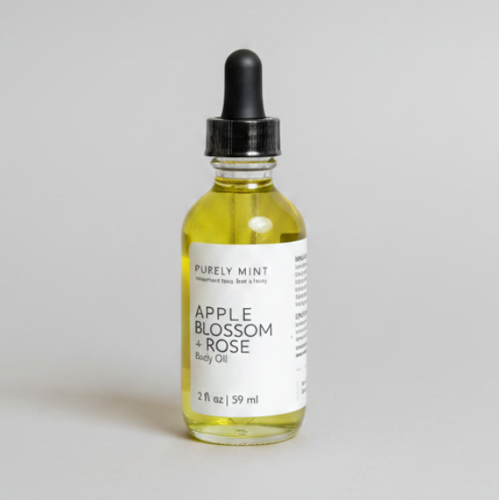 2 oz glass bottle of Apple blossom and rose body oil with black dropper top and white label on a light gray backdrop