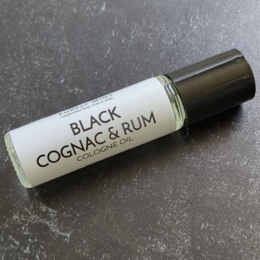 Mens Cologne Oil Roll On. A clear glass roll-on bottle with a black cap. The bottle is labeled 'PURELY MINT Hand-Crafted Soaps, Bath & Body BLACK COGNAC & RUM COLOGNE OIL'