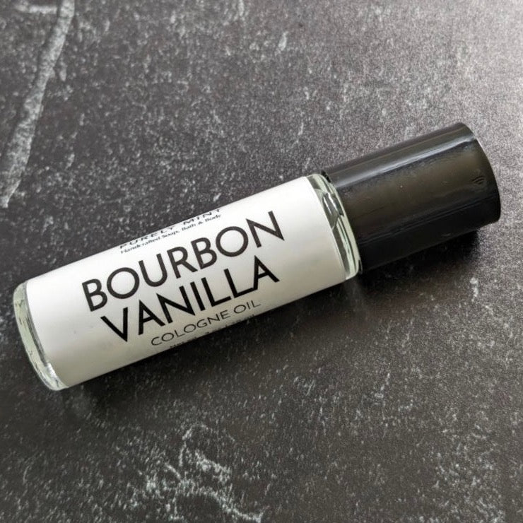 Mens Cologne Oil Roll On. A clear glass roll-on bottle with a black cap. The bottle is labeled "PURELY MINT Hand-Crafted Soaps, Bath & Body BOURBON VANILLA COLOGNE OIL"
