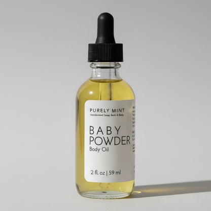 2 oz Baby Powder body oil in a glass bottle with white label and black dropper top. Light gray seamless backdrop, neutral lighting