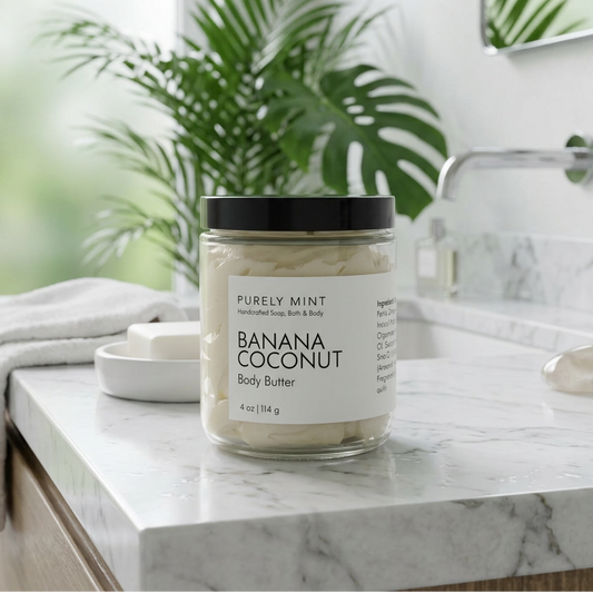 jar of Banana Coconut body butter in a modern bathroom, white marble counter, green plant. 