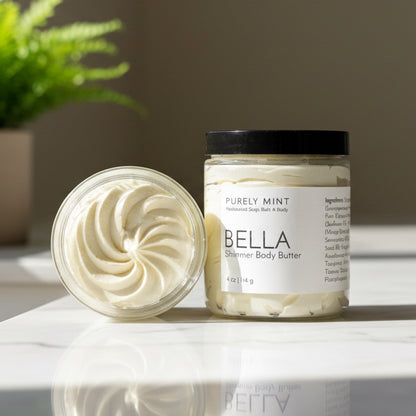 Jar of Bella body butter in a  modern bathroom, white marble counter, green plant.