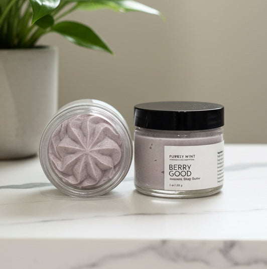 Two jars of Berry Good body butter on a white marble counter, with green plant.