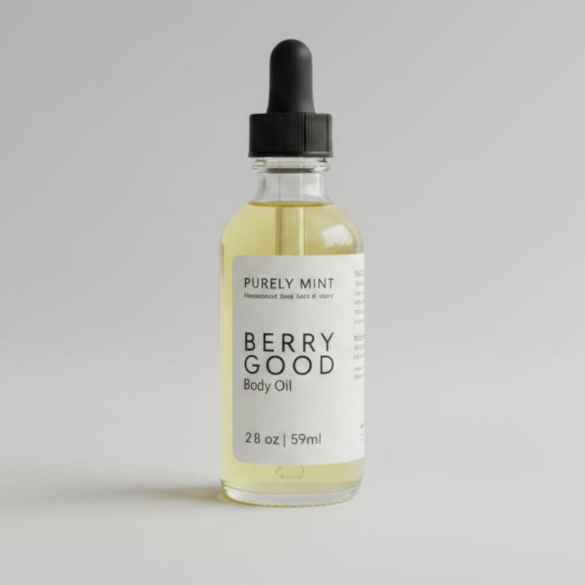 A bottle of Purely Mint Berry Good Body Oil with pale yellow oil inside, a white label, and a black cap, set against a plain bright gray backdrop background.