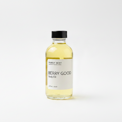 A bottle of Purely Mint Berry Good Body Oil with pale yellow oil inside, a white label, and a black cap, set against a plain white background.