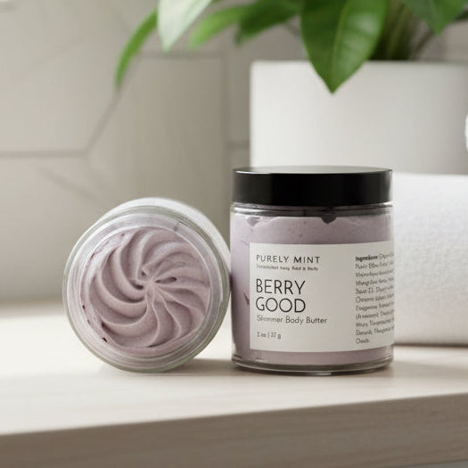 Jar of berry good body butter with a decorative swirl in a modern bathroom with a green plant.