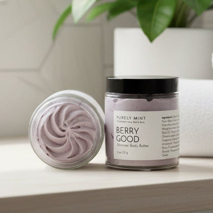 Jar of berry good body butter with a decorative swirl in a modern bathroom with a green plant.