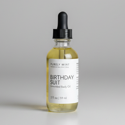 A 2 fl oz glass dropper bottle of Purely Mint Birthday Suit Unscented Body Oil, filled with pale yellow oil and featuring a white label and black dropper cap, set against a neutral gray background.