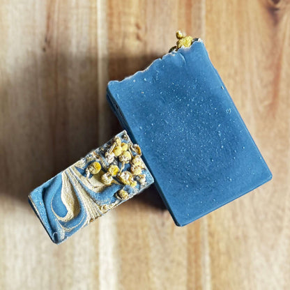 Two Black chamomile artisan soap decorative soap top and charcoal bars on a wooden surface.