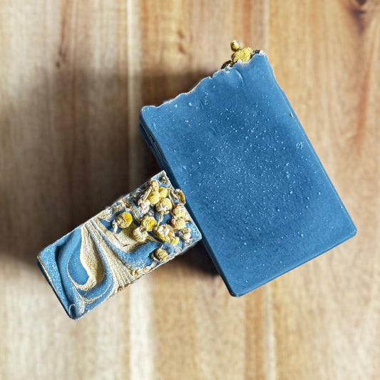 Two Black chamomile artisan soap decorative soap top and charcoal bars on a wooden surface.