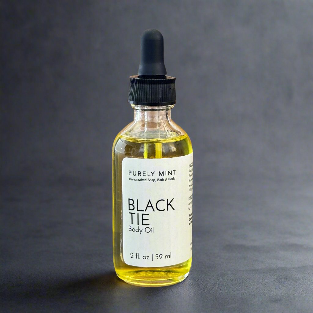 2 oz Black Tie body oil, clear glass bottle, white lable, black dropper top, commercial photography packshot, dark gray seamless backdrop.