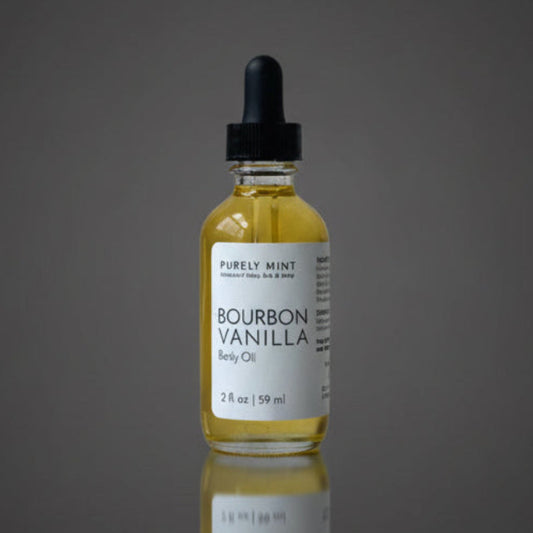 A bottle of Bourbon Vanilla body oil by Purely Mint, featuring a clear glass bottle filled with golden-yellow oil, a white label, and a black dropper cap, set against a dark gray gradient background with a reflection below.