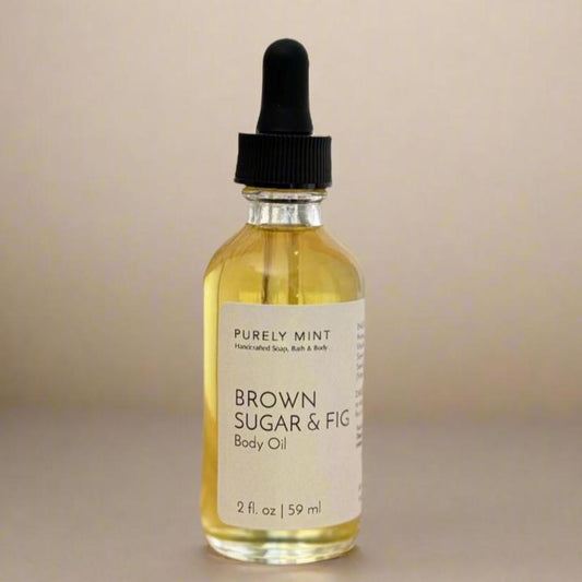 Brown Sugar & Fig Body Oil clear glass bottle, white label, black dropper top, commercial photography packshot, light cream seamless backdrop, neutral lighting.