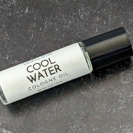 Mens Cologne Oil Roll On. A clear glass roll-on bottle with a black cap. The bottle is labeled 'PURELY MINT Hand-Crafted Soaps, Bath & Body COOL WATER COLOGNE OIL'
