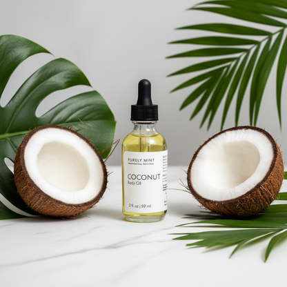 A bottle of Purely Mint Coconut Body Oil on a light marble surface, bewteen two halved coconuts and green tropical leaves against a clean white background.