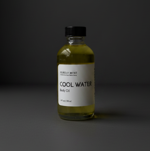 A bottle of Purely Mint 'Cool Water' body oil, featuring a clear glass bottle filled with yellow-green oil, a white label with black text, and a black cap, set against a dark gray background.