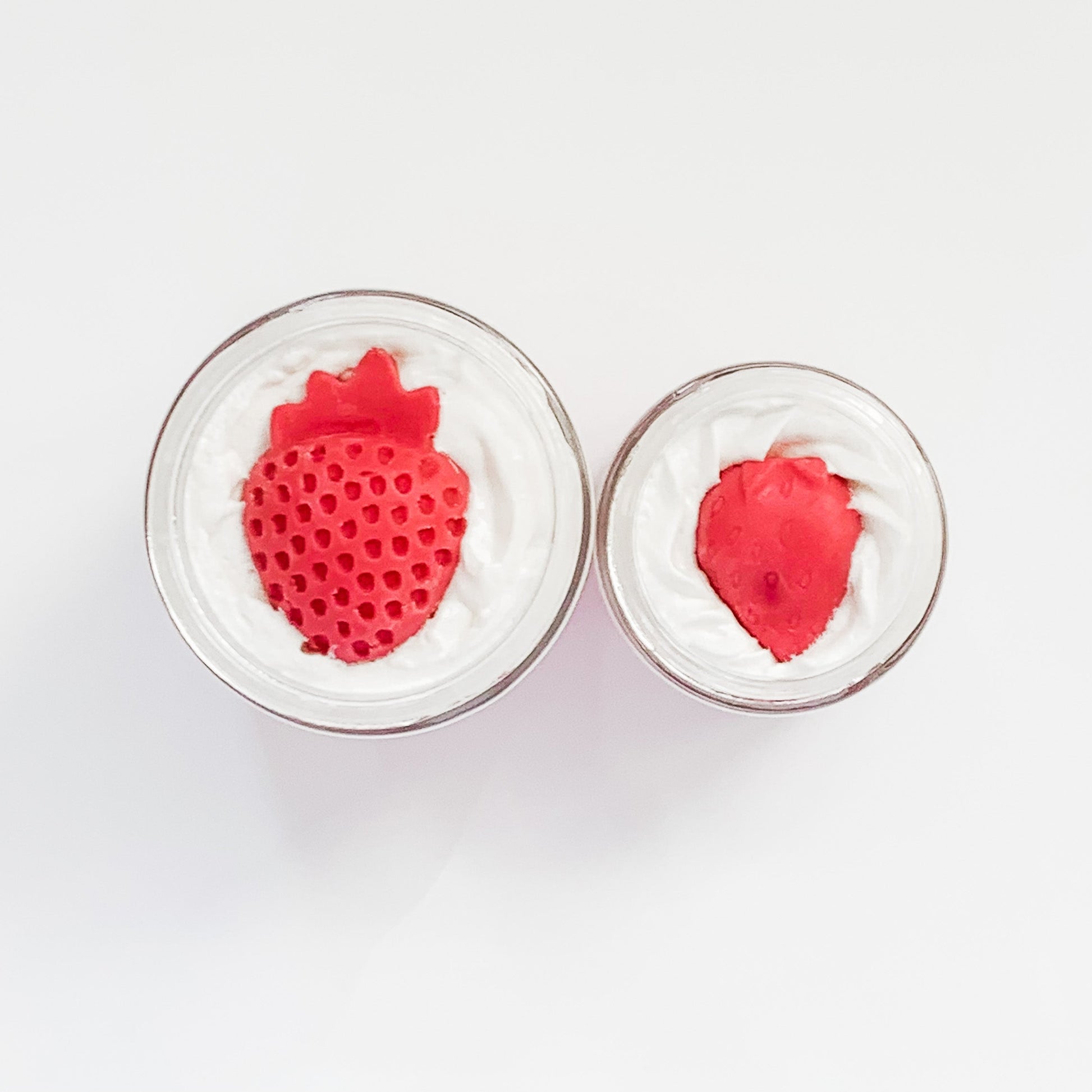 Two red strawberry-shaped objects in clear containers on a white background