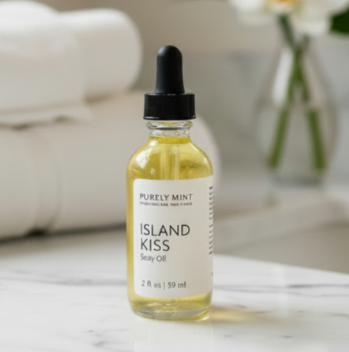 A bottle of Purely Mint Island Kiss Body Oil with a black dropper cap and white label, set on a white marble surface with a blurred spa-like background.
