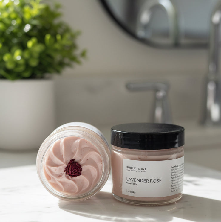 2 jars of Lavender Rose body butter in a modern bathroom, white marble counter, green plant. body butter is pink with a swirled top with a rose in the center.