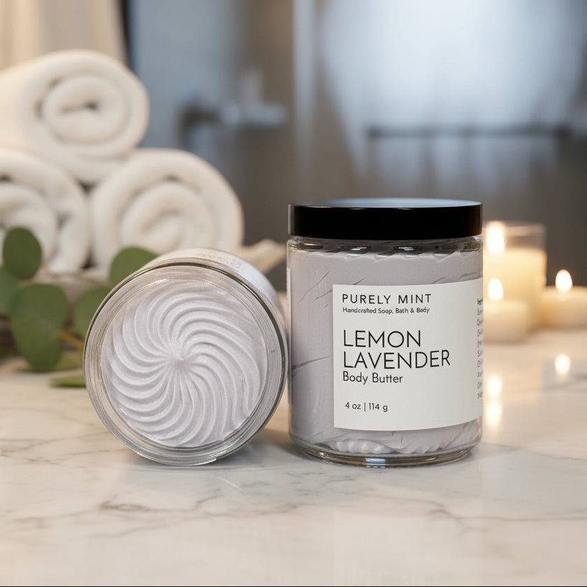 Lemon Lavender body butter in a luxury bathroom with rolled white washcloths, candles and a green plant on a marble counter. 