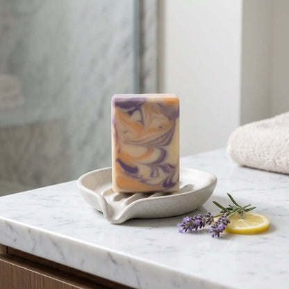 yellow and purple Lemon lavender artisan soap on a soap dish in a bathroom with a towel and lemon and lavender accents in the background