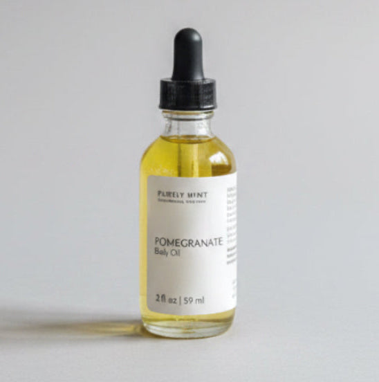 A small 2 oz glass dropper bottle of pomegranate body oil with a white label and black dropper cap, standing on a natural gray backdrop.