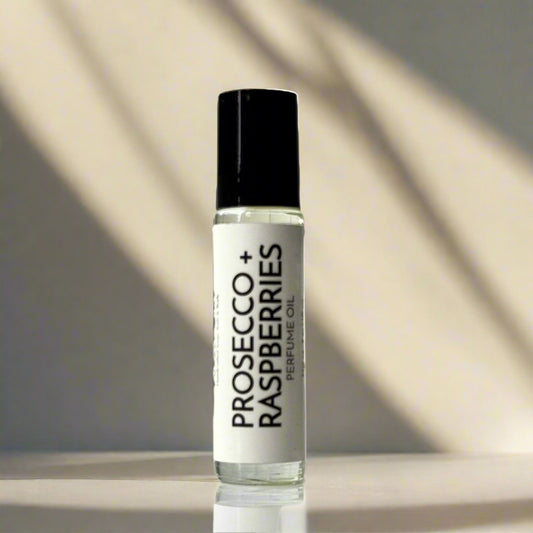 Perfume oil bottle labeled 'Prosecco + Raspberries' on a light tan background