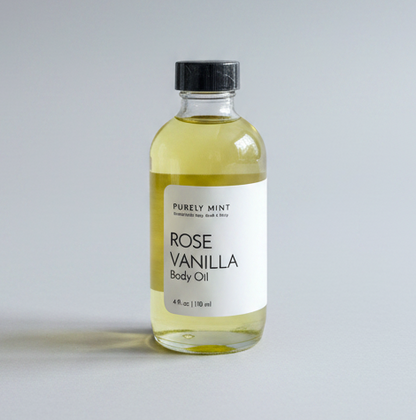 A 2 oz glass dropper bottle of Rose Vanilla Body Oil with a white label and black dropper cap, placed on a light gray backdrop. 