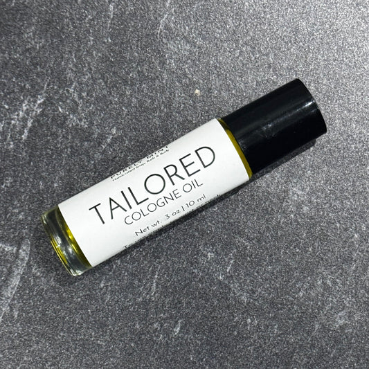 A 10 ml roll-on bottle of Tailored Cologne Oil by Purely Mint, featuring a white label and black cap, resting on a textured gray stone surface.