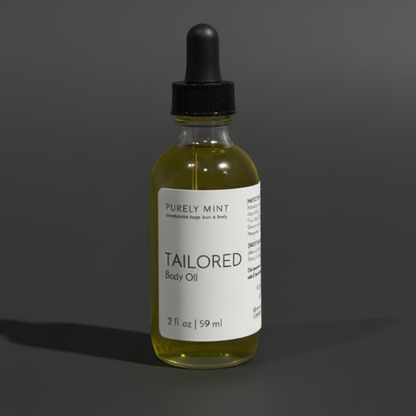 A small glass dropper bottle of body oil with a black cap and white label reading 'PURELY MINT' and 'TAILORED Body Oil,' centered on a dark gray studio background.