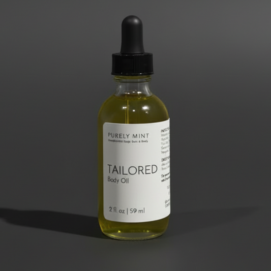 A small glass dropper bottle of body oil with a black cap and white label reading 'PURELY MINT' and 'TAILORED Body Oil,' centered on a dark gray studio background.