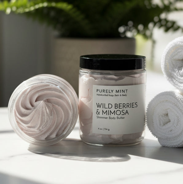 Jar of Purely Mint Wild Berries & Mimosa shimmer body butter in a modern bathroom, white marble counter,  green plant, rolled white washcloths.