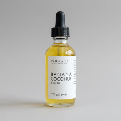 Bottle of Banana Coconut Body Oil on a commercial photography packshot, light gray seamless backdrop, neutral lighting.