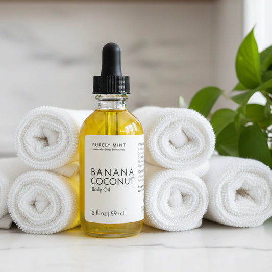 Bottle of Banana coconut body oil in spa setting with white marble counter rolled wash clothes green plant