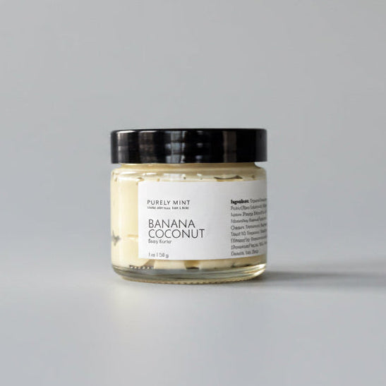 Jar of 'Banana Coconut' body butter on a dark surface with a gray background
