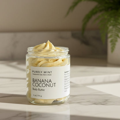 Jar of Banana Coconut yellow body butter with on a white marble counter with a green plant.