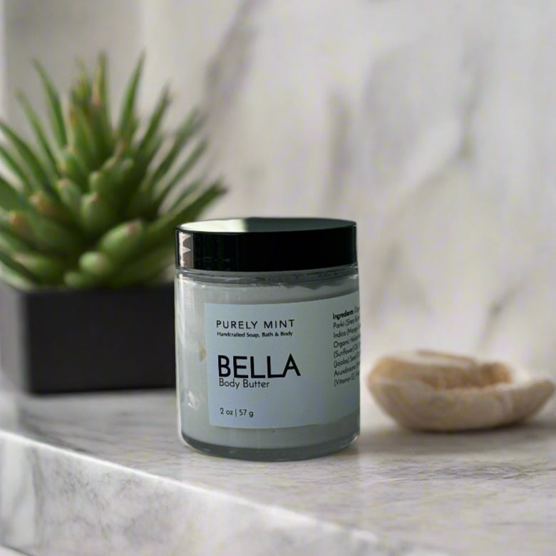 Jar of Bella body butter on a reflective surface with a blurred background