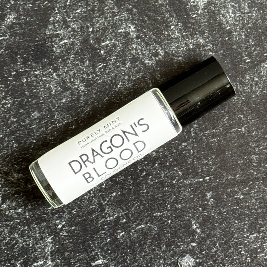 A clear roller bottle with a black top of Dragon's Blood cologne oil on a dark textured surface